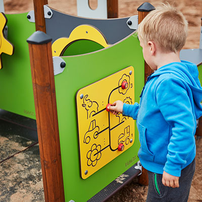 A young boy interacts with a play panel at a playground which is a maze to find animals with a lever.